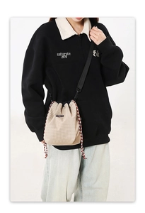 Detailed view of beige grid bucket bag with tricolor drawstring worn by model