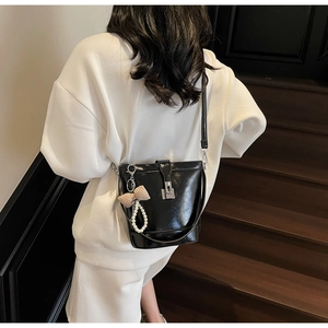 Glossy black bucket bag with pearl charm and bow shown on a model on a staircase