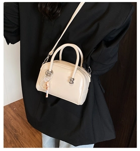 Detail of a cream faux leather boston bag with pearl chain and cartoon pendant accessory