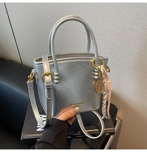 Detailed shot of silver bucket bag with metallic texture, gold logo, and tennis racket charm