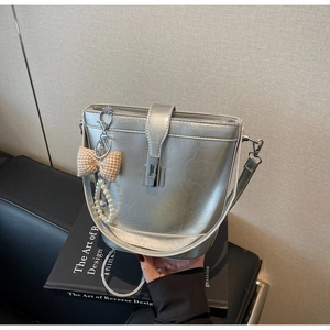 Detail of silver bucket bag with vintage texture, metal clasp, and pearl bow charm