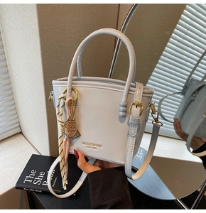 Detail of light blue bucket bag with gold hardware, tennis charm and striped ribbon