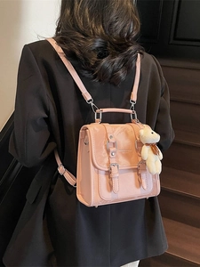 Pink faux leather fashion backpack with bear pendant worn by model in a street style view