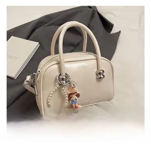 Detail of cream Boston bag with pearl chain and doll pendant on soft lifestyle background
