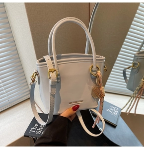 Detail of grey-blue bucket bag featuring a gold logo, tennis racket charm and silk scarf