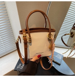 Detail of white and brown contrast bucket bag with logo print and metal ring charm