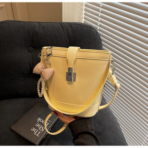 Detail of light yellow PU leather bucket bag with bow charm and pearl chain decoration