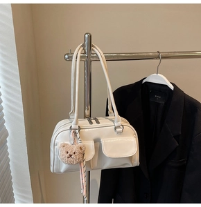 Detail einer weißen Lackleder-Schultertasche mit Teddy-Anhänger an einem Metallbügel