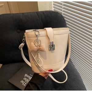Detail of cream PU bucket bag with plaid bow charm and pearl chain on velvet background