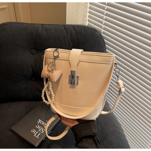 Detail of cream bucket bag with metal buckle, plaid bow, and pearl charm on sofa