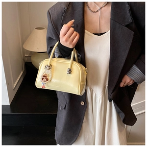 Detail of glossy yellow Boston bag with pearl charm shown with professional styling