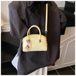 Detail of light yellow Boston bag with silver studs and a pearl girl charm accessory