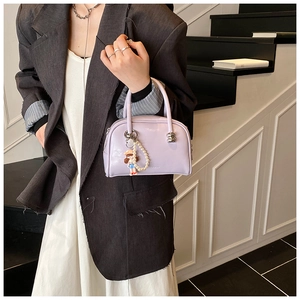 Detail of lavender patent leather shell bag with pearl chain and doll on grey blazer