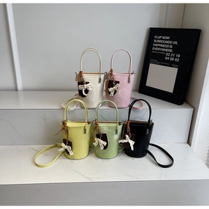 Collection of five colorful leather bucket bags with bow charms on marble surface