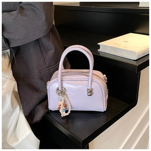 Detail of a purple leather Boston bag with a pearl doll charm on a display stand