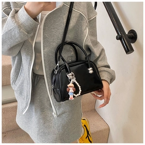Detail of black glossy handbag featuring silver hardware and a pearl cartoon doll charm