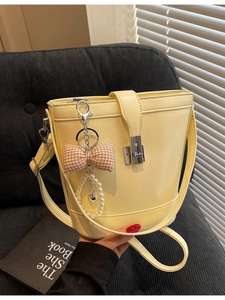 Creamy yellow bucket bag with ribbon and pearl charms on a grey fabric surface