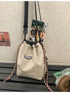 Beige checkered drawstring bucket bag with adjustable black strap and side woven detail