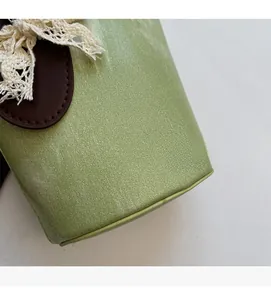 Detail of light green bucket bag with brown leather trim and white lace bow decoration