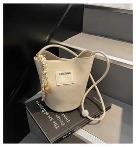 Détail du sac seau blanc cassé avec grain litchi, étiquette de marque et nœud décoratif