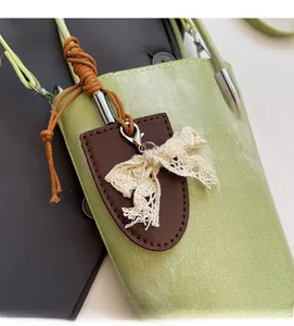 Detail of light green bucket bag with brown leather tag and cream lace bow charm