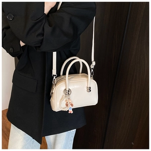 Chic off-white mini Boston bag with pearl chain and doll charm worn with a blazer