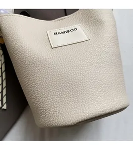 Détail du sac seau beige avec texture grainée et écusson du logo HAMIROO