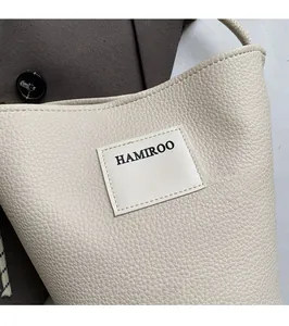 Détail du logo HAMIROO sur un sac seau en cuir grainé blanc cassé élégant