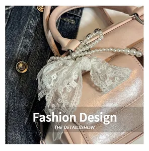 Close-up of pink patent leather handbag with pearl charm and white lace bow detail