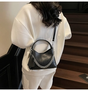 Detail of black lychee texture bucket bag with silver chain strap shown on a model