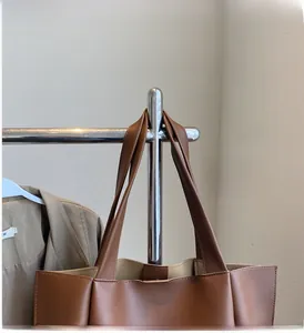 Detail of wide reinforced leather handles on a brown minimalist tote bag with stitching