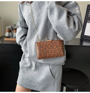 Dettaglio borsa leopardata con tracolla a catena dorata e chiusura metallica su legno scuro