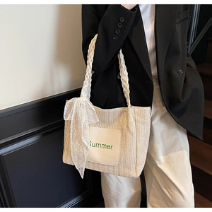 Detail of woven straw tote bag with green Summer text and white lace bow accessory