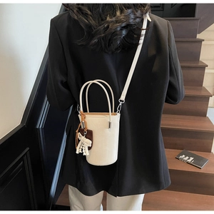 Minimalist beige bucket bag worn as a crossbody by model on a wooden staircase