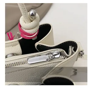 Detail view of smooth silver metal zipper and woven knotted handle on a beige leather bag