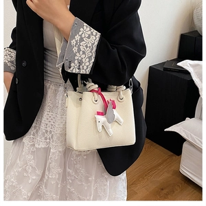 Close-up of cream textured leather bucket bag with knotted handle and horse charm