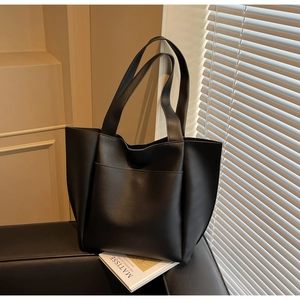 Detail shot of a large black matte leather tote bag with wide straps and front pocket