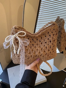 Handwoven straw beach bag with hollow floral patterns and a pearl ribbon charm