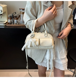 Detail of off-white bowling bag with dual front pockets and decorative lace bow charm