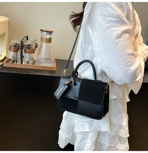 Black patchwork handbag with gold metal handle and strap worn by a model