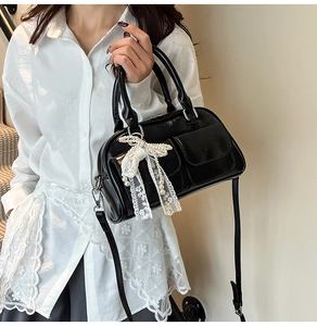 Detail of black glossy leather bag featuring a delicate lace bow and pearl charm