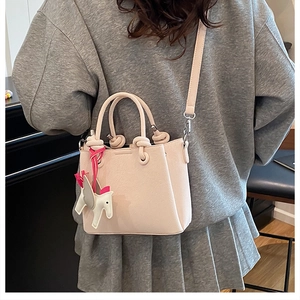 Detailed back view of a beige crossbody bucket bag with horse charm on a model
