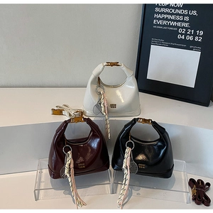 Three glossy patent leather dumpling bags in white, burgundy, and black with tennis charms