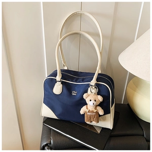 Détail du sac bowling bleu marine et crème avec une peluche d'ours sur un siège en cuir