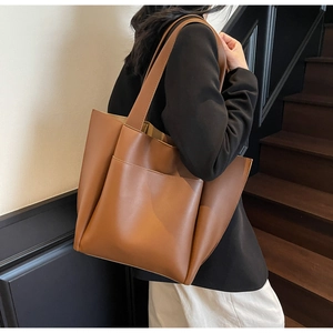 Close-up of brown leather tote bag with front pocket showing stitching and shoulder strap
