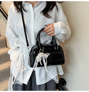 Detail of a black glossy mini bowling bag with lace bow and pearl charm accessory