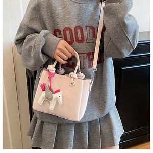 Detail of light pink leather crossbody bag with a cute white pony charm accessory
