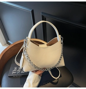 Detail of off-white leather bag with lychee texture and silver chain on wooden chair