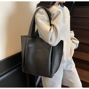Close-up of a black leather tote bag with wide shoulder strap and external side pocket