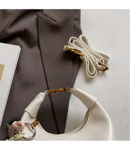 Detail of white glossy crescent bag with gold buckle and woven strap ornament